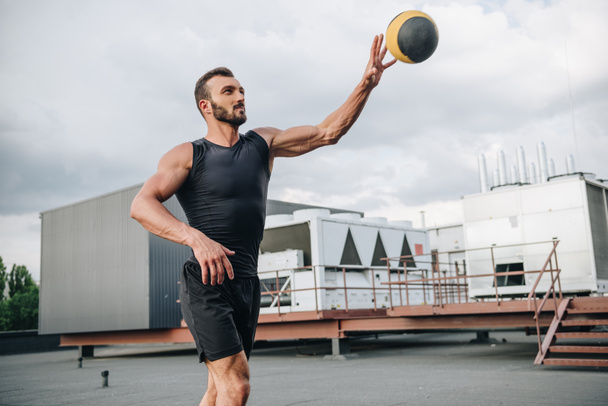 handsome sportsman training with medicine ball on roof - Photo, Image