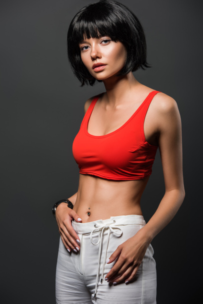 slim young woman in red crop top looking at camera isolated on grey - Photo, Image