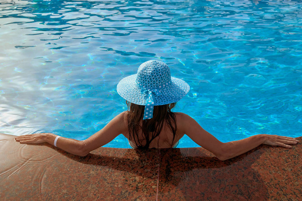 屋外スイミング プール夏の端、リラックスと旅行の概念の上に座って帽子で美しい女性 - 写真・画像