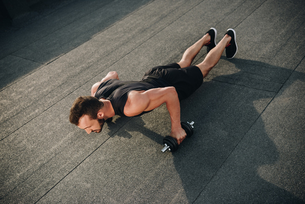 high angle view of handsome sportsman doing push ups with dumbbells on roof - Photo, Image