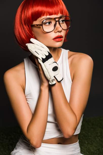 seductive young woman with red bobbed haircut in golf glove and stylish eyeglasses looking away on grey - Φωτογραφία, εικόνα