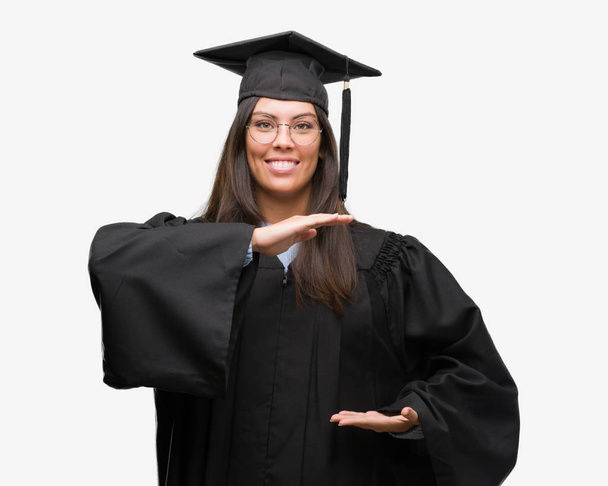 Jonge Spaanse vrouw, die is afgestudeerd aan GLB en uniform gebaren met de handen tonen grote en groot formaat teken, symbool van de maatregel. Glimlachend kijken naar de camera. Meten concept. - Foto, afbeelding