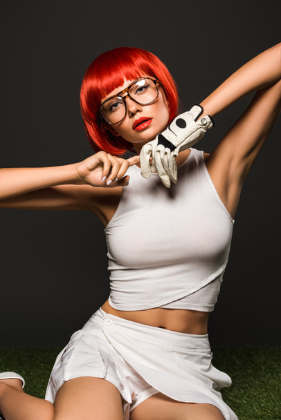 seductora joven con bob rojo cortado en guante de golf y gafas con estilo mirando a la cámara en gris
 - Foto, imagen