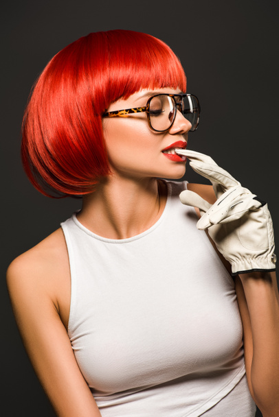 seductive young woman with red bob cut in golf glove and stylish eyeglasses isolated on grey - Fotografie, Obrázek