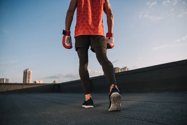 cropped image of sportsman walking with boxing gloves on roof - Foto, afbeelding