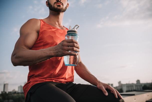 cropped image of sportsman holding sport bottle of water on roof - Zdjęcie, obraz