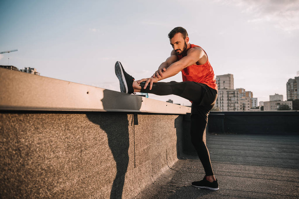 handsome sportsman stretching legs on roof - Photo, Image
