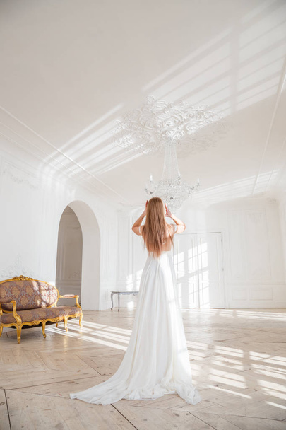 Colpo di moda di bella donna bionda in abito bianco in piedi contro sfondo interno bianco
 - Foto, immagini