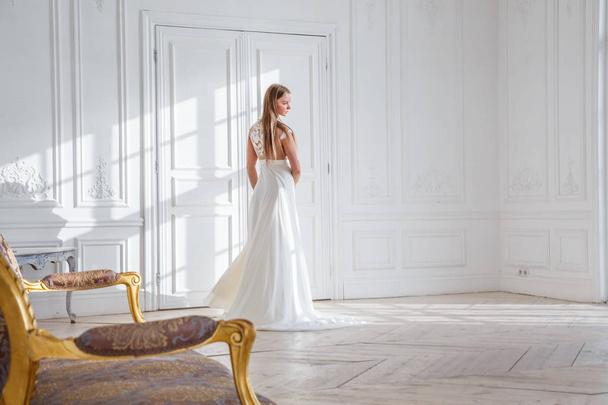 Fashion shot of beautiful blonde woman in white dress standing against white interior background - Foto, Imagem