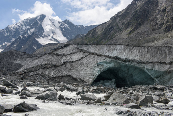 The Akkem River flows from the glacier at the foot of Belukha Mountain. In the background, snow tops. In the foreground the stream runs among the stones. - 写真・画像