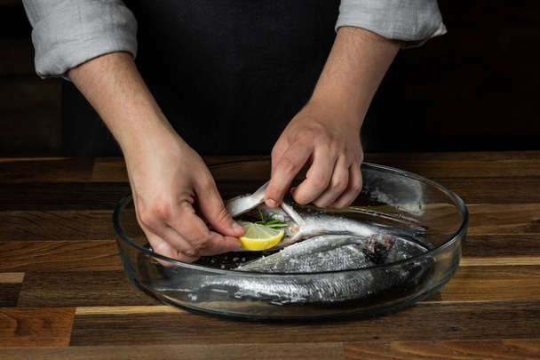 Cuoco cucina pesce di mare con condimento su tavola di legno
 - Foto, immagini