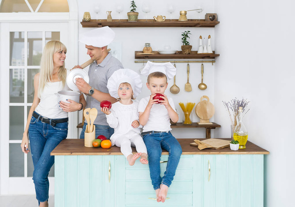 Kaukasische en gelukkige familie in witte caps met twee kinderen is in eigen keuken. Kinderen, culinaire en mensen concept. - Foto, afbeelding