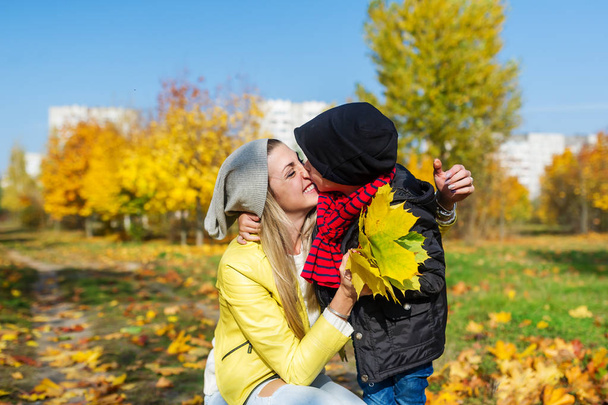Мать и маленький сын гуляют в осеннем парке. Ребенок нежно обнимает и целует маму.
 - Фото, изображение