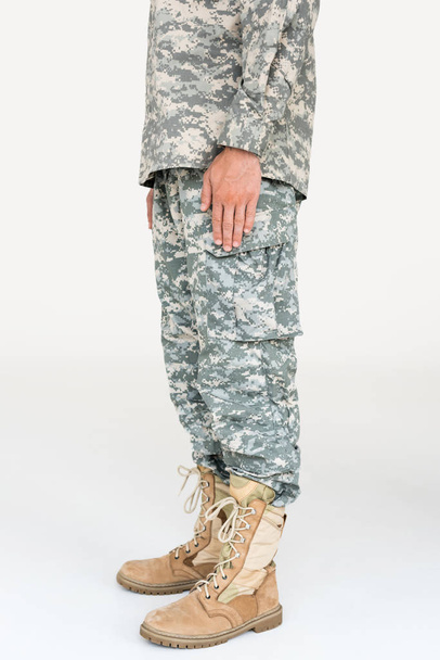 partial view of male soldier in camouflage clothing and boots on grey background - 写真・画像