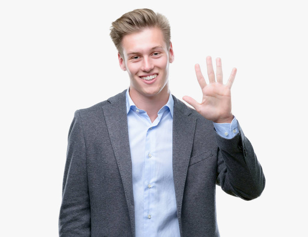 Молодой привлекательный блондин-бизнесмен появляется и показывает пальцем номер пять, улыбаясь уверенно и счастливо.
. - Фото, изображение