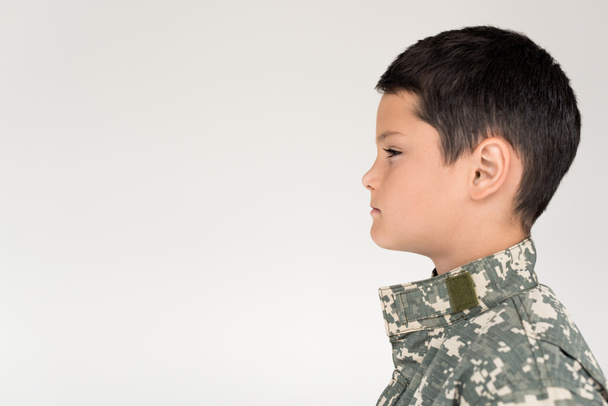 вид сбоку ребенка в военной форме, отводящего взгляд на сером фоне
 - Фото, изображение