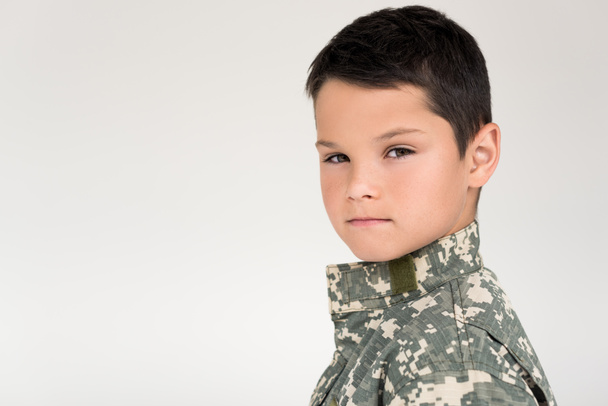 side view of kid in military uniform looking at camera on grey background - Foto, Imagen