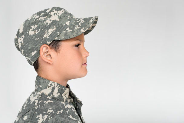 Widok z boku z małym dzieckiem w wojskowym mundurze pozowanie na szarym tle - Zdjęcie, obraz