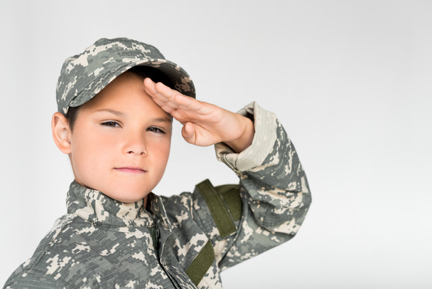 portrait of little kid in military uniform saluting on grey background - Φωτογραφία, εικόνα