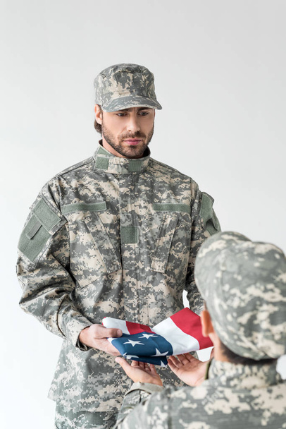 partial view of soldier giving folded american flag to kid in camouflage clothing on grey background - Фото, изображение