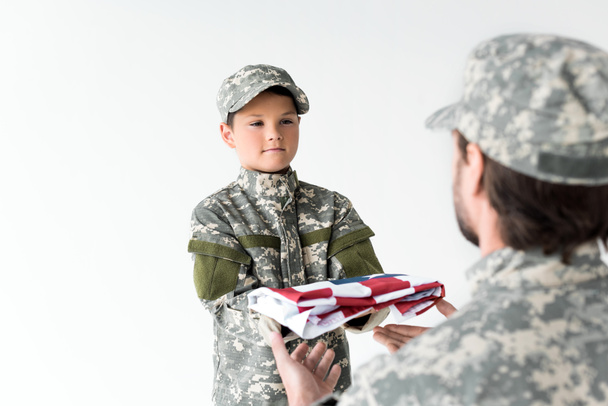 vue partielle du petit garçon vêtu de camouflage donnant un drapeau américain plié au soldat sur fond gris
 - Photo, image