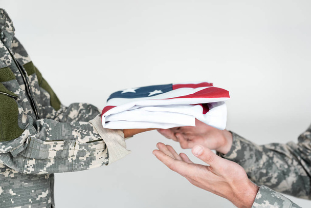 cropped shot of kid in camouflage clothing giving folded american flag to soldier on grey background - Φωτογραφία, εικόνα
