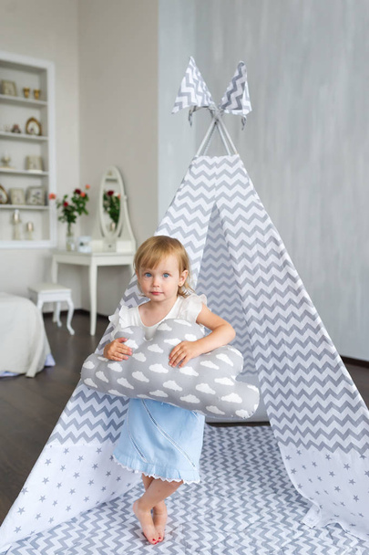 Portrait of little beautiful girl with pillow standing in teepee at nursery room. - Photo, Image