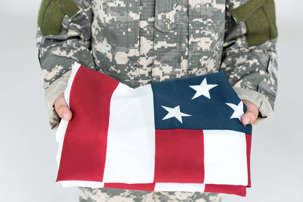 colpo ritagliato del capretto in uniforme militare che tiene la bandiera americana piegata nelle mani isolate su grigio
 - Foto, immagini