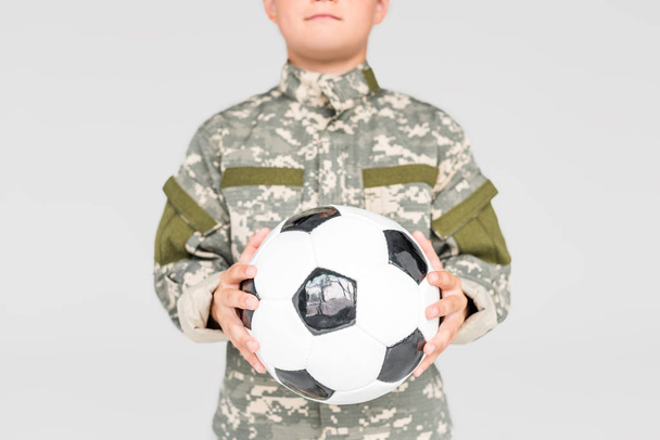 частичный взгляд ребенка в военной форме с футбольным мячом в руках, изолированных на сером
 - Фото, изображение