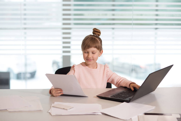 young girl businesswoman in casual clothes, sitting at a table closely look at documents, working at computer - Foto, Imagem