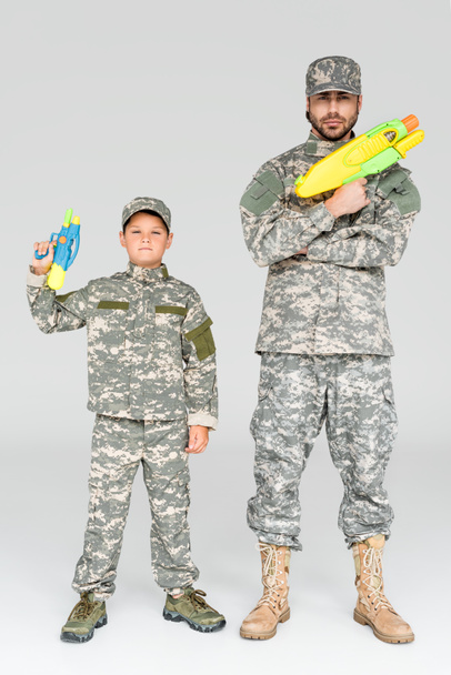 apa és fia, katonai egyenruhában játék víz fegyvereket a szürke háttér - Fotó, kép