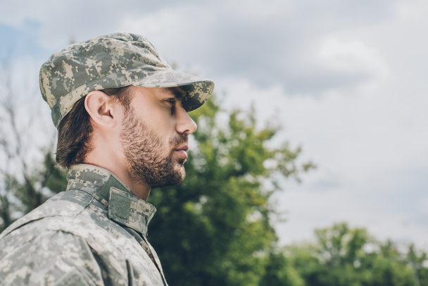 vista lateral de soldado confiado en uniforme militar con cielo nublado en el fondo
 - Foto, imagen