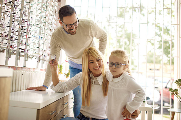 Happy family choosing glasses in optics store.  - Foto, Bild