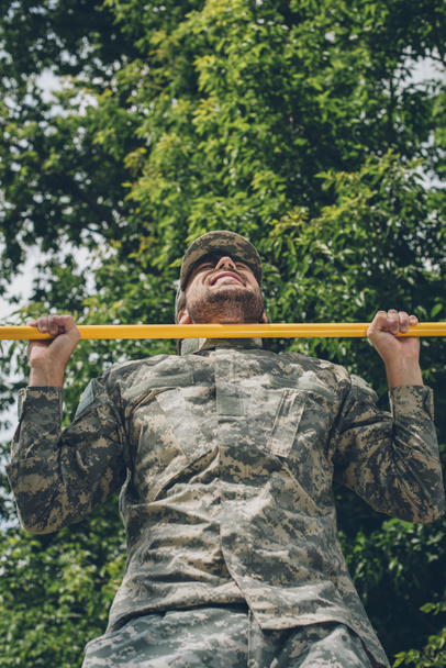 low angle view of soldier in military uniform pulling himself up on crossbar - Photo, Image