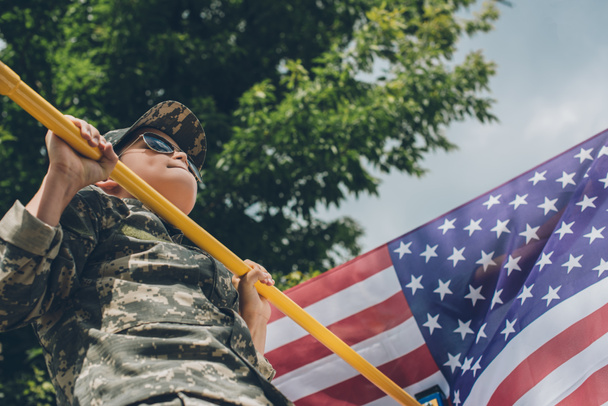 low angle view of boy in sunglasses pulling himself up on crossbar with american flag on backdrop - Fotoğraf, Görsel