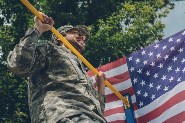 baixo ângulo de visão do soldado puxando-se na barra transversal com bandeira americana em pano de fundo
 - Foto, Imagem