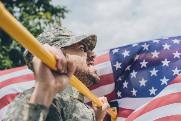 Πλάγια όψη του στρατιώτη σηκώνοντας ο ίδιος στο οριζόντιο δοκάρι με αμερικανική σημαία στο φόντο - Φωτογραφία, εικόνα