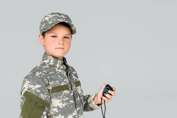 portrait of kid in military uniform with stop watch in hand looking at camera isolated on grey - Photo, image