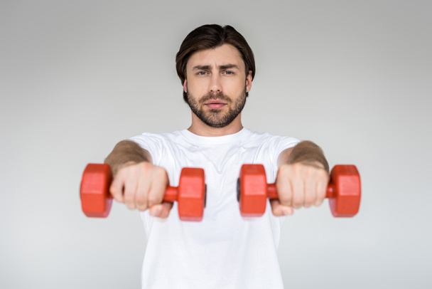 portrait of man in white shirt with red dumbbells in hands exercising on grey backdrop - Fotografie, Obrázek