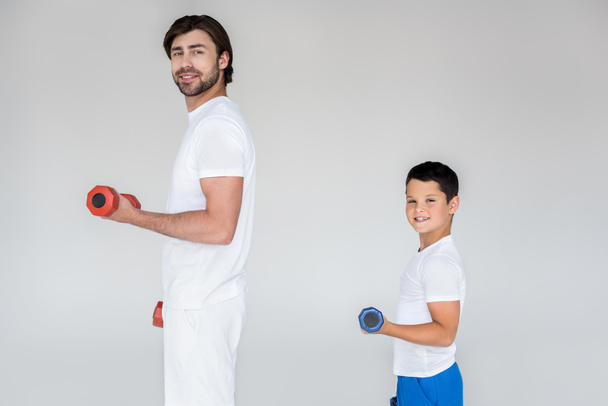 sivukuva hymyilevästä isästä ja pojasta valkoisissa paidoissa, jotka käyttävät käsipainoja harmaalla pohjalla
 - Valokuva, kuva