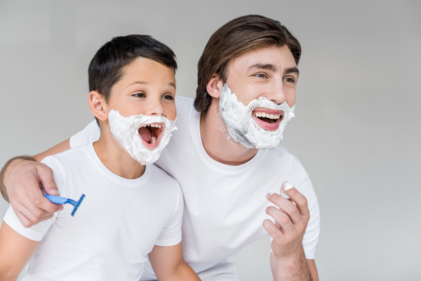excited father and son with shaving foam on faces isolated on grey - Foto, afbeelding
