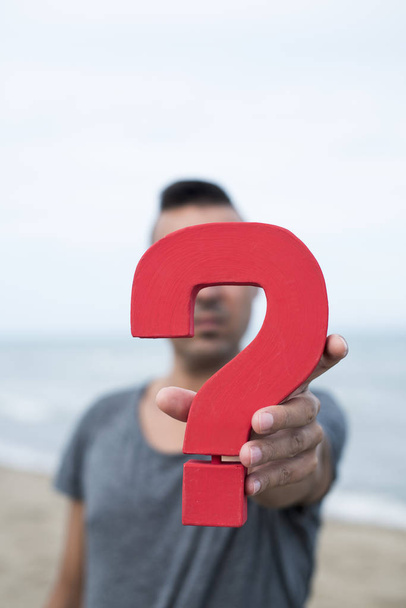 closeup of a young caucasian person with a question mark in front of her or his face, with the ocean in the background - Photo, Image