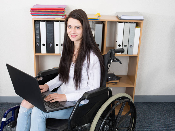 Young disabled woman in wheelchair working at office building - Фото, изображение