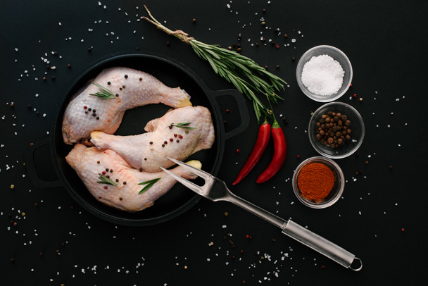 επίπεδη lay με πόδια κοτόπουλου στην κατσαρόλα με μπαχαρικά και πιρούνι το κρέας στον μαύρο πίνακα  - Φωτογραφία, εικόνα