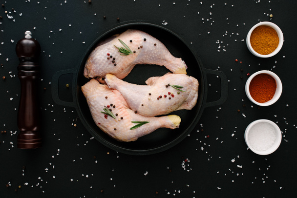 flach mit Hühnerkeulen auf Pfanne mit Pfefferkörnern und Paprika auf schwarzem Tisch  - Foto, Bild
