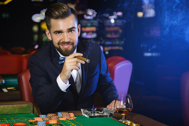 Rich handsome man smoking cigar and playing roulette in the casino - Φωτογραφία, εικόνα