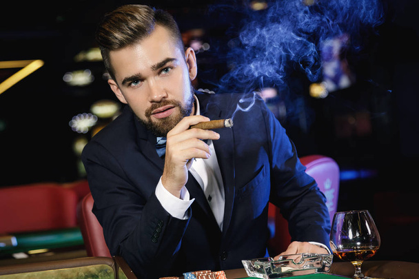 Rich handsome man smoking cigar and playing roulette in the casino - Фото, зображення