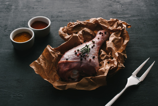 raw turkey leg with pepper corns on baking paper on wooden table with paprika spices - Fotó, kép