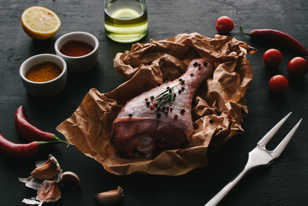 one turkey leg with pepper corns on baking paper on wooden tabletop with vegetables and spices - Fotoğraf, Görsel