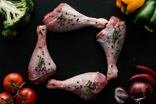 top view of raw turkey legs with pepper corns, rosemary and different vegetables on wooden black table - Foto, immagini